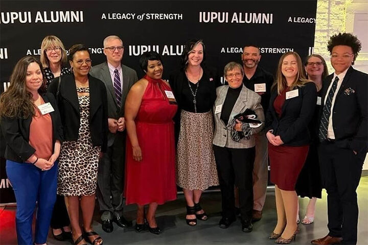 A group of School of Liberal Arts alumni pose in front of a Liberal Arts banner.